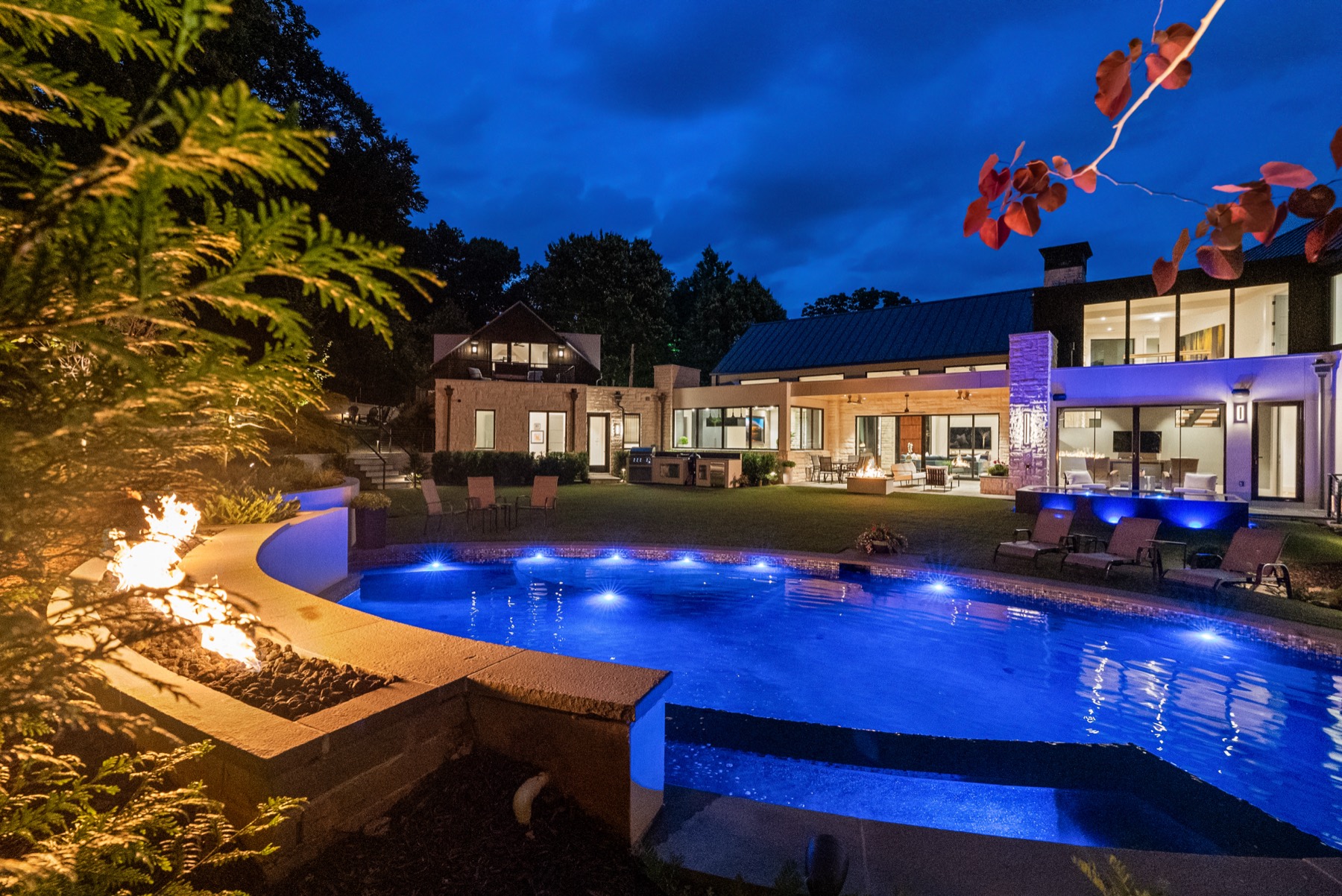 Twilight exterior of an Atlanta home with a curved illuminated pool and fire pit